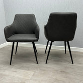 Two modern gray upholstered dining chairs with black legs, set against a textured gray wall on a neutral floor.